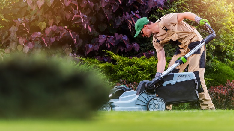 Man in beige clothing using electric lawn mower