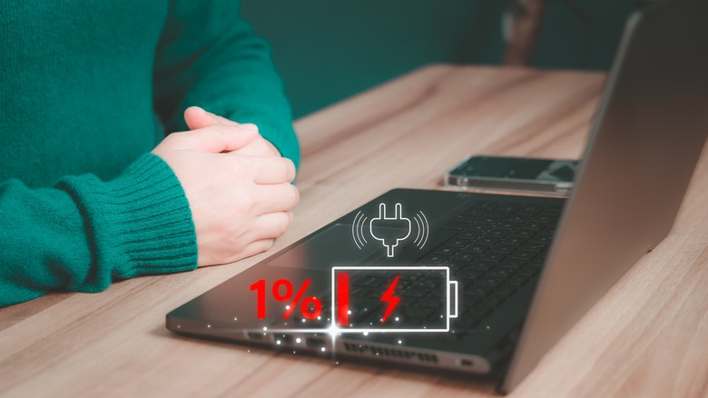 A laptop on a wooden desk with low battery icon over it