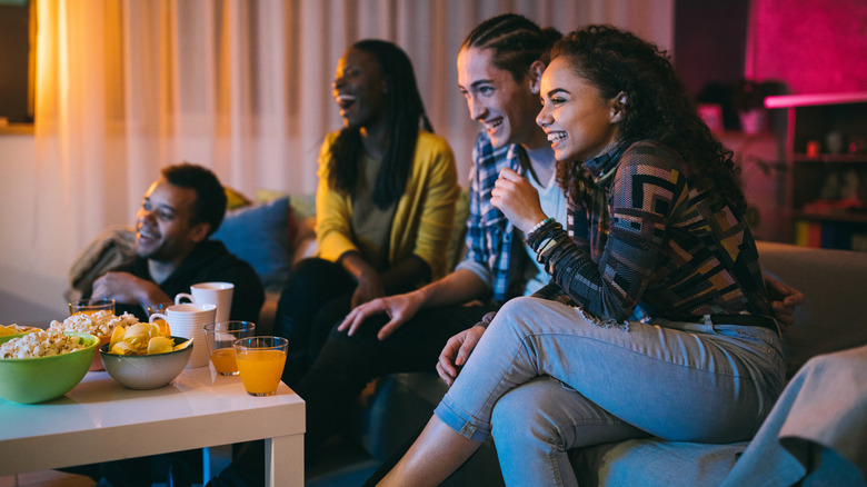 Four friends watching TV together and enjoying snacks and beverages