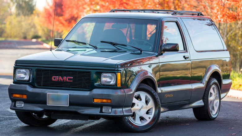 A 1993 Forest Green Metallic with Gray GMC Typhoon high-performance SUV is pictured against a background of fall foliage