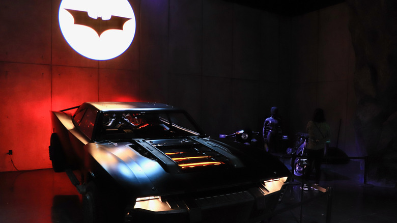 A batmobile with the Batman logo on the wall behind