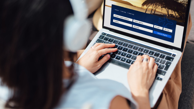 A faceless woman is searching for flights on her laptop