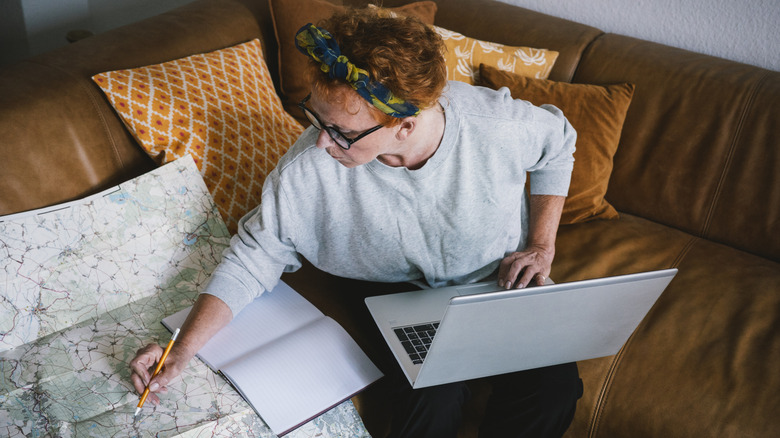 A woman is making travel plans using a physical map and a laptop