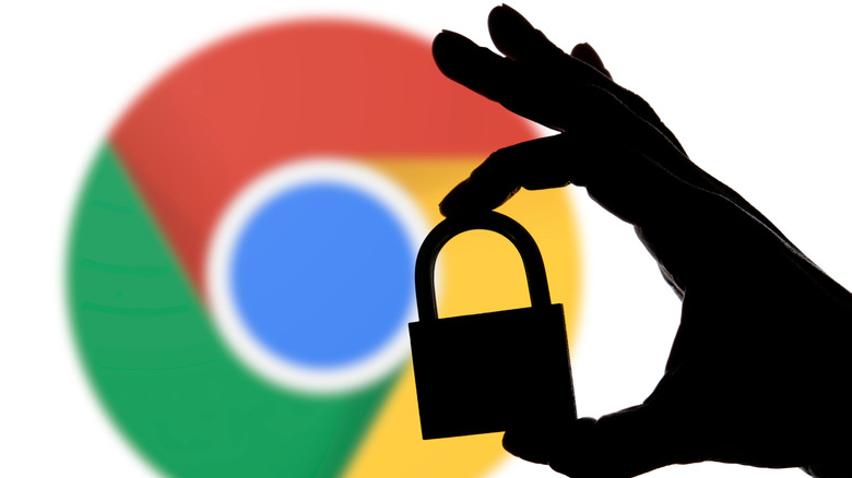 A silhouette of a hand holding a padlock in front of a large slightly out-of-focus chrome logo