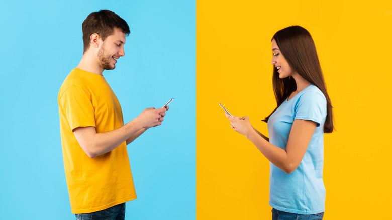 A man and a woman both typing on cellphones facing one another. The man is wearing a yellow shirt and is front of a blue background. The woman is wearing a blue shirt in front of a yellow background.