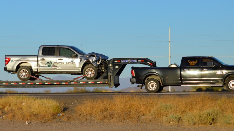 Pickup hauling wrecked police truck on flatbed