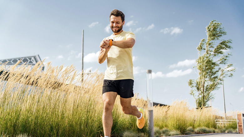 Happy man checking progress on fitness watch while running