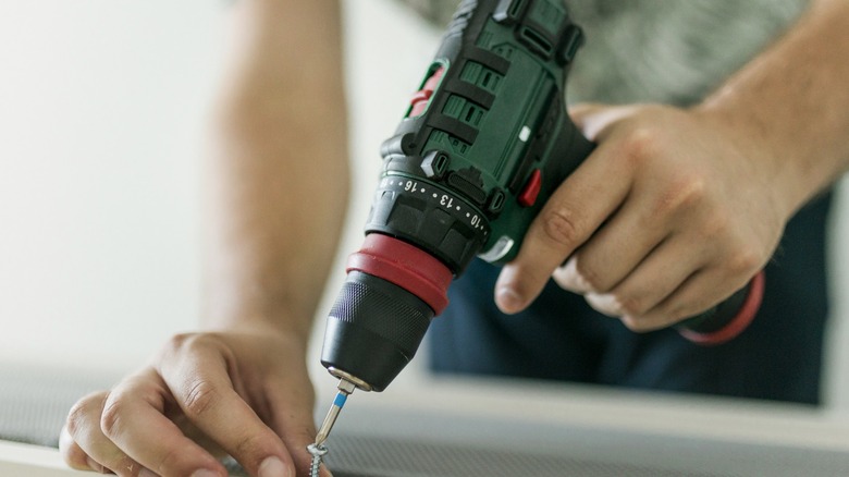 Green drill being used to screw in screw