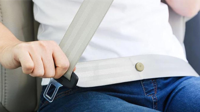 A small button is visible on a seat belt being put on by a person