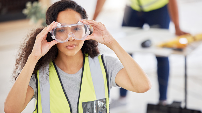 Woman on construction job puts on safety goggles