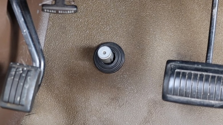 Image of a high beam button on the floorboard of a classic car to the left of the brake pedal.