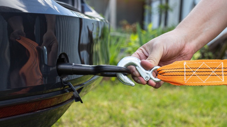 A hand attaching a hook to a car's tow eye hook