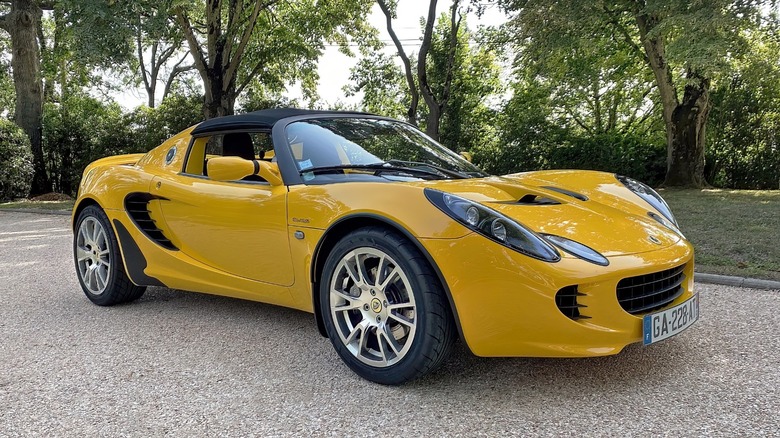 A yellow Series 2 Lotus Elise Type 111 sits in front of trees