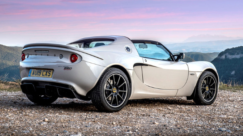 A white Lotus Elise stands in front of mountains and a reddish-blue sky