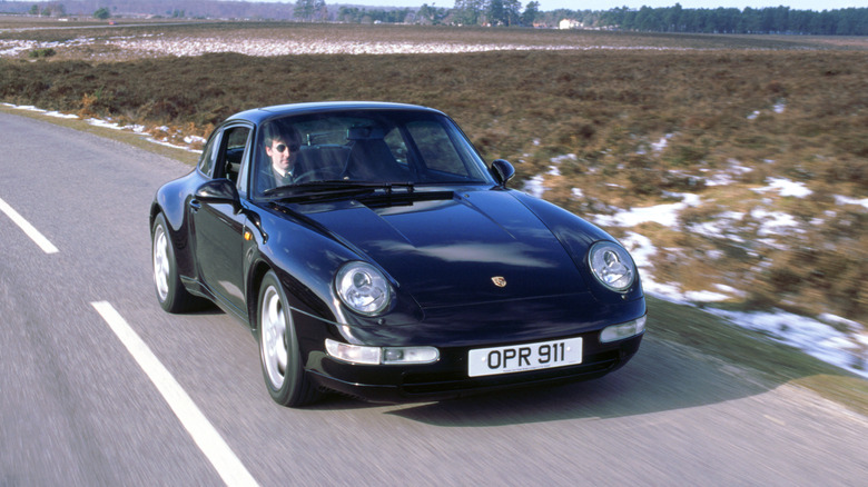 A black Porsche 993 driving on country roads