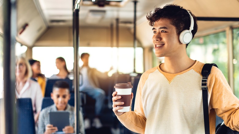 Man wearing a white and yellow shirt on a bus with headphones on.