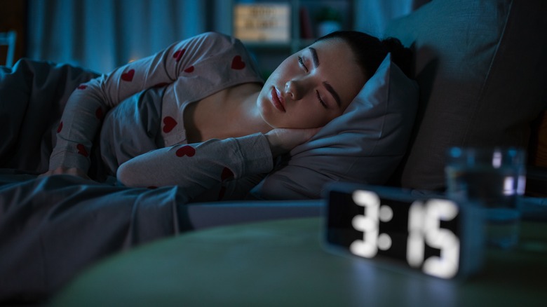 Woman sleeping on a bed next to an alarm clock.