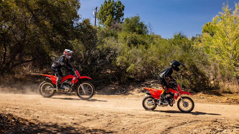 Adult and child riding Honda dirt bikes on a dusty road