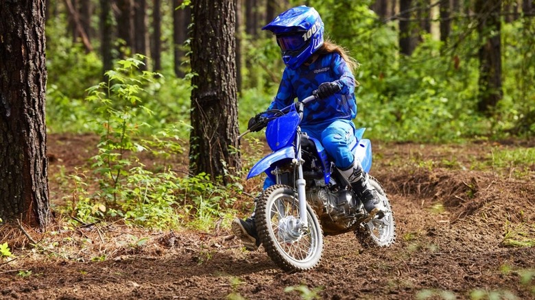 Young person riding a Yamaha TT-R110E on a wooded track