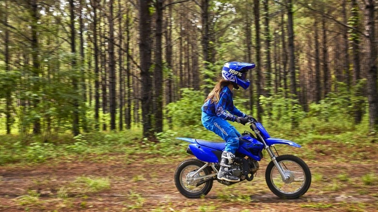 A youngster riding a Yamaha TT-R110E through a forest 