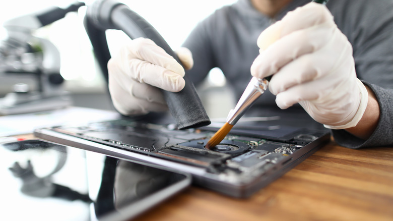 Someone cleaning the inner-workings of a laptop with a brush and vacuum