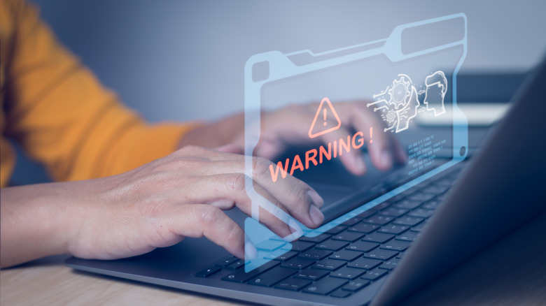 Person using laptop with digital render of warning message overlaid