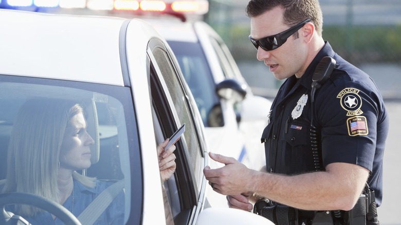 A driver hands her license to a sunglasses-wearing police officer