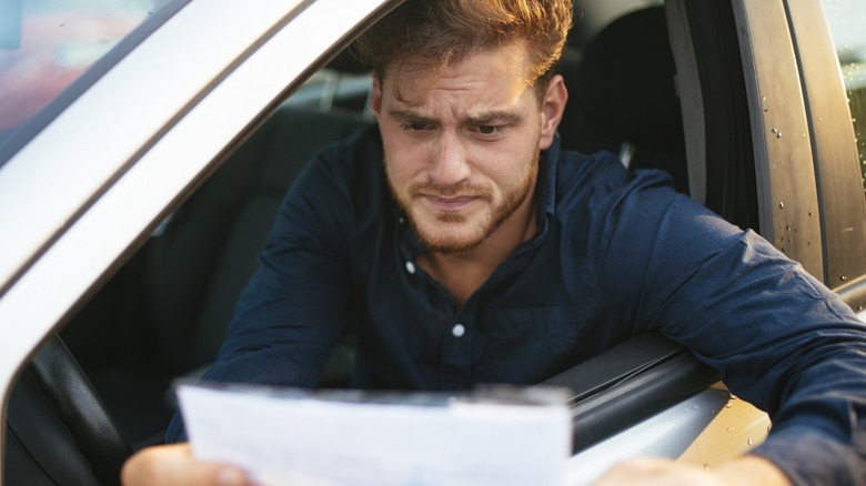 A driver grimaces as he looks at a traffic ticket