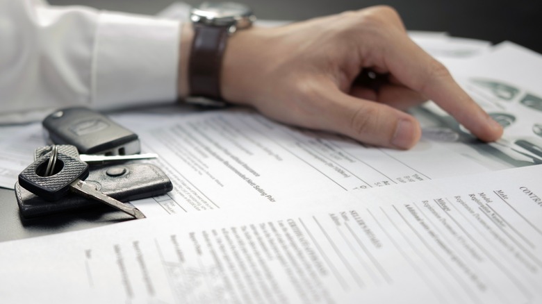 A hand points to a document with car keys resting on it