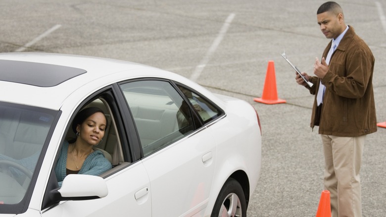 A driving school instructor looks at a driver who's trying to navigate around orange cones