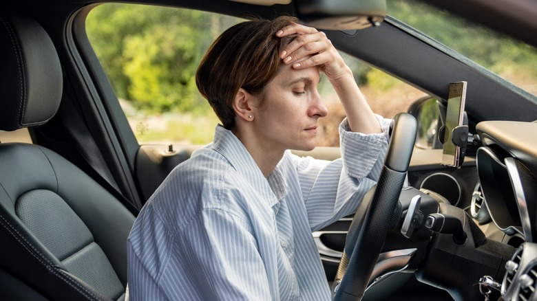 A driver sits in her car with her eyes closed, a hand on her forehead