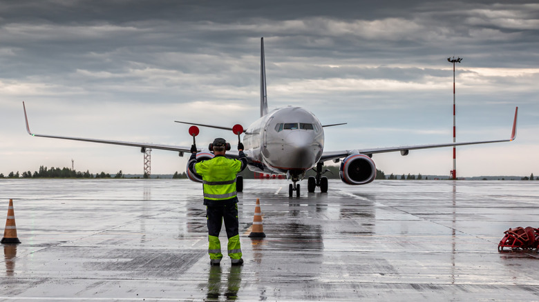 A commercial airliner being directed where to go on a wet runway.