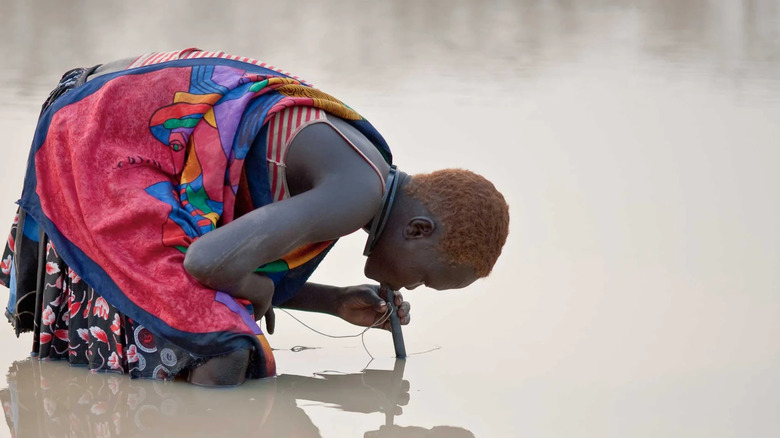 woman drinking via LifeStraw in a murky river