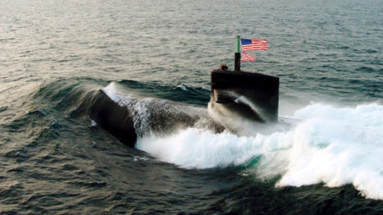 A U.S. submarine surfacing at sea, flag flying.