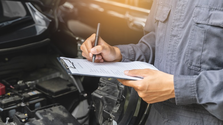 mechanic with clipboard near car engine