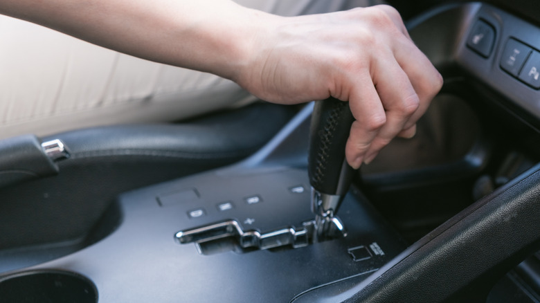 A driver holds on to the shift lever of an automatic transmission.