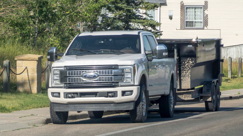 White Ford F250 pickup towing black construction trailer in suburban area