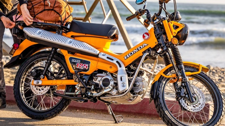 A person attaching bags to a yellow Honda Trail125.