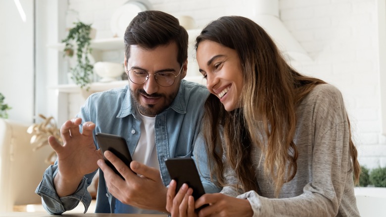 A couple using their phones and smiling