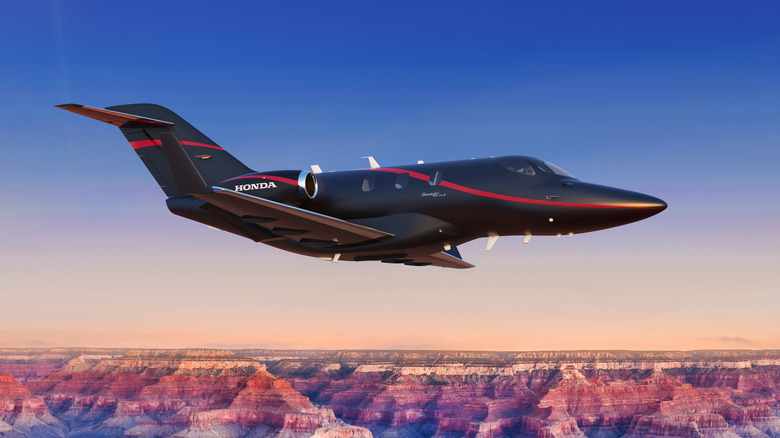 A Black HondaJet Elite II private aircraft flying over canyon lands.