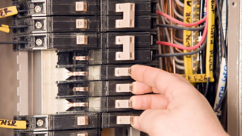 A Close Up Of Residential Circuit Breakers With A Hand Positioned To Flip Three Of Them To The On Position