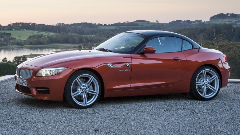 2013 BMW Z4 parked on a paved surface with tree-covered hills and a water body in the background