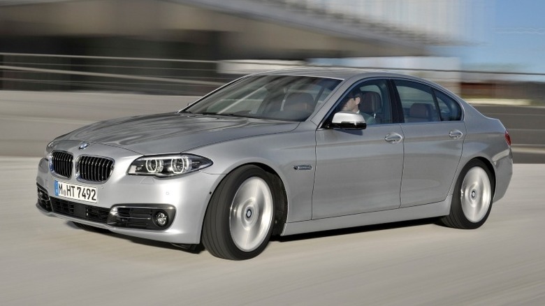 2013 BMW 5 Series driving down city street with a blurred building in the background