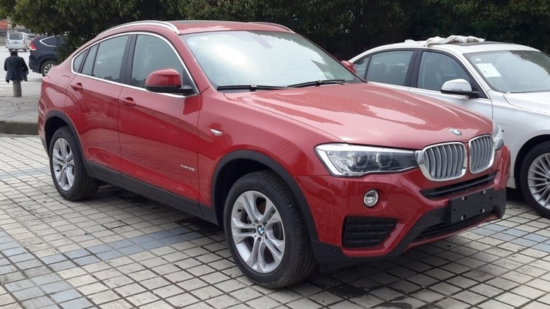 Red BMW F26 X4 xDrive28i parked on a paved concrete surface with a tree in the background