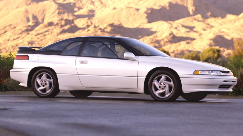 A white Subaru SVX parked with a rocky background