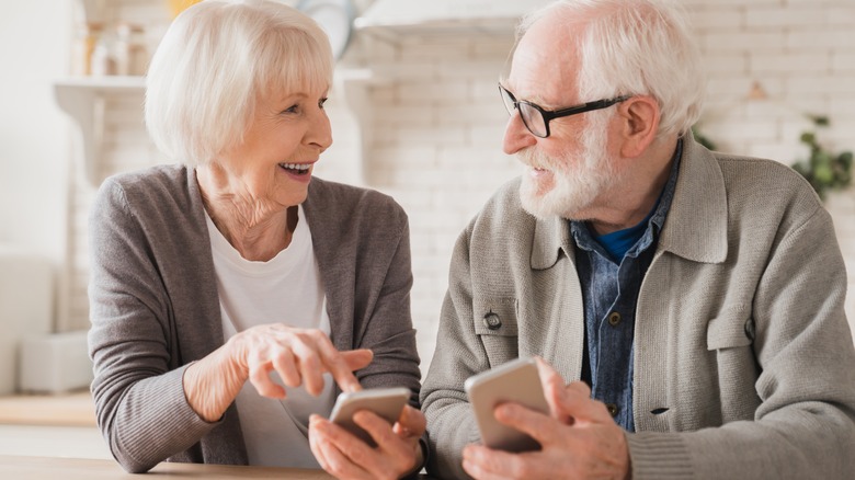 gray haired couple holding smartphones