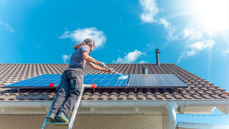 A man on a ladder cleaning solar panels with a mop.