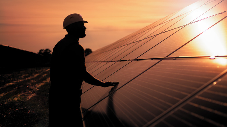 Silhouette of a man inspecting a solar panel.