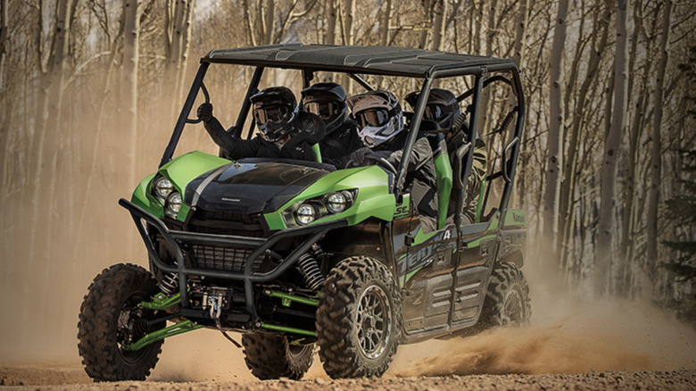 four riders in green and black Kawasaki Teryx 4 on dirt road in woods