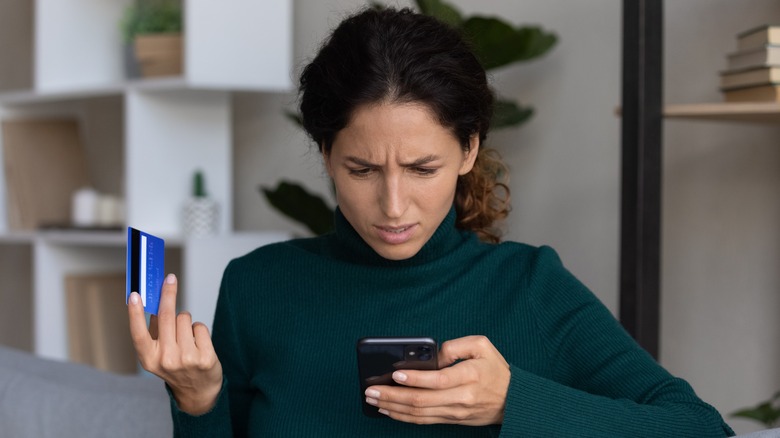 Upset, looking at phone with credit card in-hand